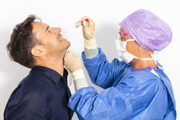 Um médico de fato de proteção que toma um esfregaço nasal de uma pessoa para testar uma possível infecção por coronavírus - Foto, Imagem