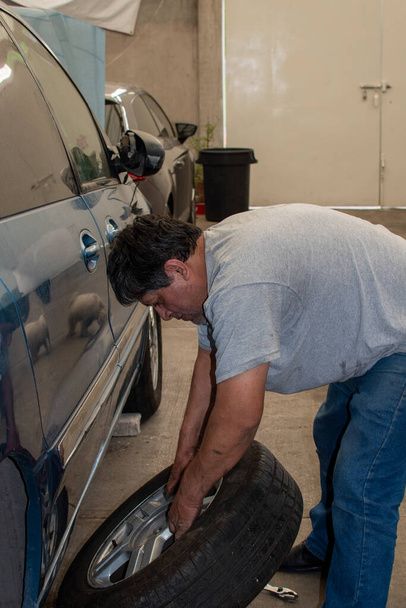 hombre cambiando una rueda de un camión azul usando solo herramientas de mano
 - Foto, imagen