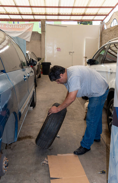 homem mudando uma roda de um caminhão azul usando apenas ferramentas manuais
 - Foto, Imagem