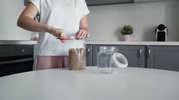 Woman pours buckwheat into a glass jar for storage. - Filmati, video