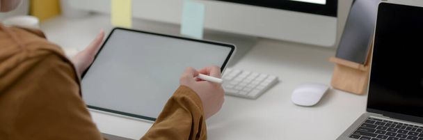 Vista de perto de freelancer feminino trabalhando em tablet de tela em branco na mesa branca com outros dispositivos digitais no escritório em casa
 - Foto, Imagem