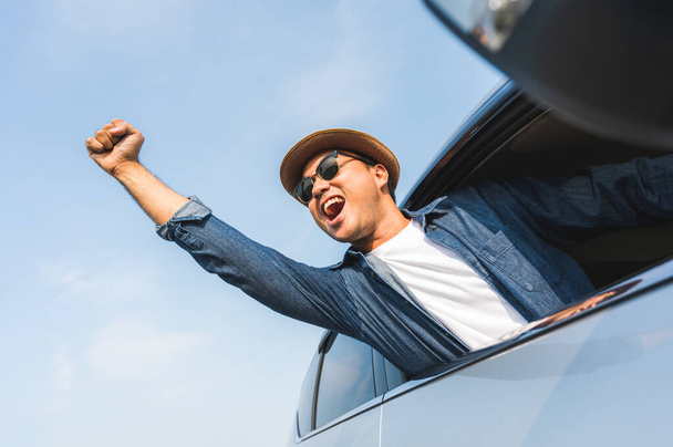 An Asian man is enjoying his trip. He stretches out of the car window to make him look happy. - Foto, Bild