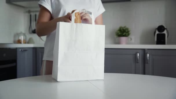 Nő kipakolás bevásárló táska kenyér, zabpehely, tej, zöldségek a konyhában a fa asztalon. Nulla hulladék otthon és ökotáska. Öko-vásárlás. - Felvétel, videó