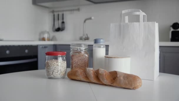 Unverpackte Einkaufstasche mit Brot, Haferflocken, Buchweizen, Milch, Gemüse auf Holztisch in der Küche. Zero waste home und eco bag. Öko-Einkauf. - Filmmaterial, Video
