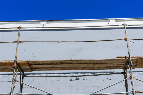 Vue rapprochée d'échafaudages métalliques rouillés avec plate-forme en bois de travail à côté du mur du bâtiment industriel
 - Photo, image