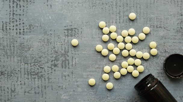 yellow round tablets or pills vitamins flat lay on blue stone concrete table with black plastic bottle, top down view, horizontal stock photo image still life background with copy space - 写真・画像