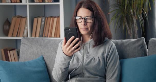 Beautiful woman in earphones having video chat on smartphone - Video, Çekim