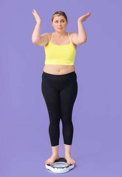Displeased overweight woman on scales against color background. Weight loss concept - Fotografie, Obrázek