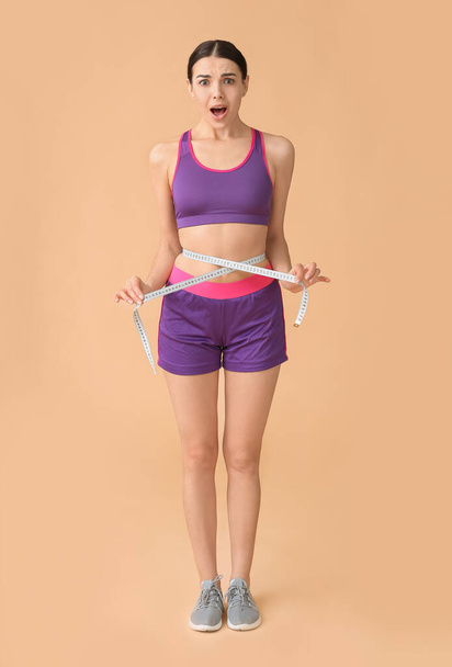 Jeune femme choquée avec ruban à mesurer sur fond de couleur. Concept de perte de poids
 - Photo, image