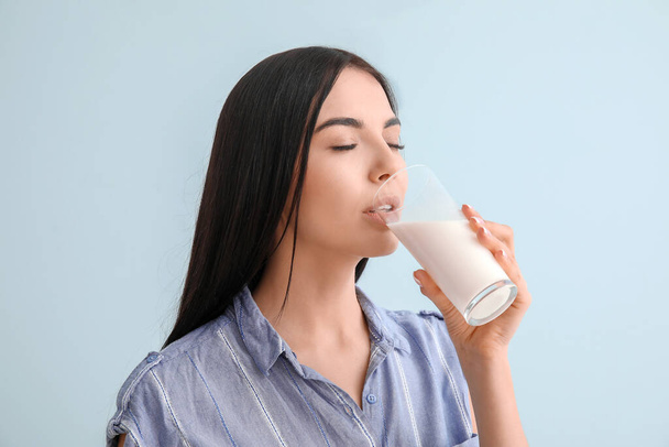 Красивая молодая женщина пьет молоко на цветном фоне
 - Фото, изображение