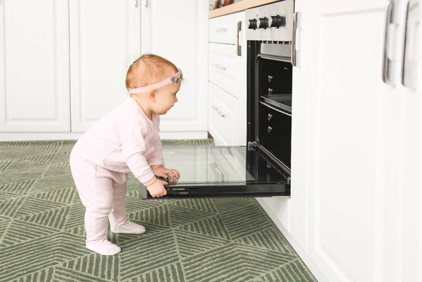 Μικρό μωρό κοντά στο φούρνο στην κουζίνα. Το παιδί κινδυνεύει. - Φωτογραφία, εικόνα