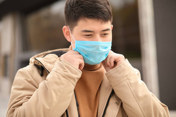 Hombre asiático con máscara protectora en la calle de la ciudad. Concepto de epidemia
 - Foto, imagen