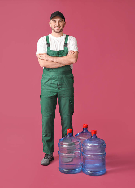 Delivery man with bottles of water on color background - Fotoğraf, Görsel