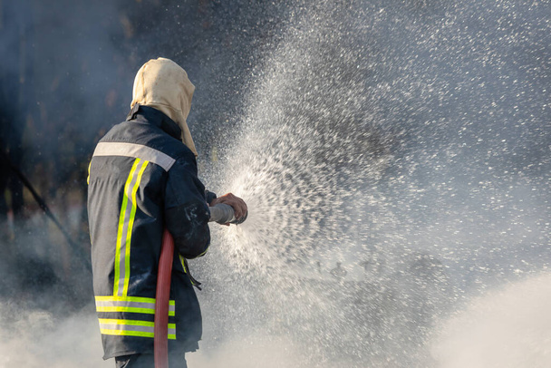 Feuerwehrmann oder Feuerwehrmann versprüht Wasser aus großem Wasserschlauch, um Brand zu verhindern - Foto, Bild