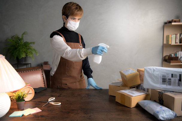 Una persona rociando desinfectante en paquetes y cajas durante la pandemia del coronavirus Covid-19
 - Foto, Imagen
