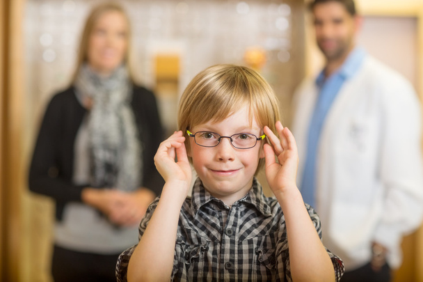 Boy Trying Glasses With Optometrist And Mother At Store - 写真・画像