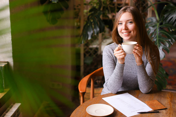 Молода усміхнена дівчина п'є чай, візову заявку та паспорт на столі
. - Фото, зображення