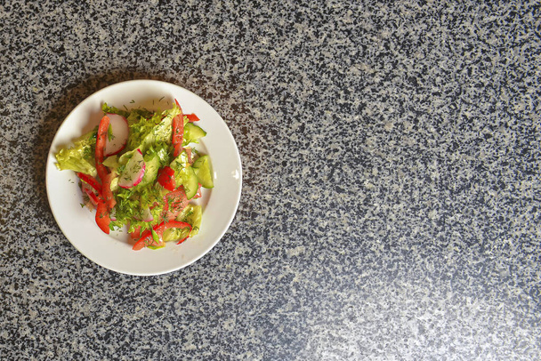 Vegetable salad with radishes,cucumber, sweet pepper and dill. Served in a white plate over grey textured table. - Foto, Imagem
