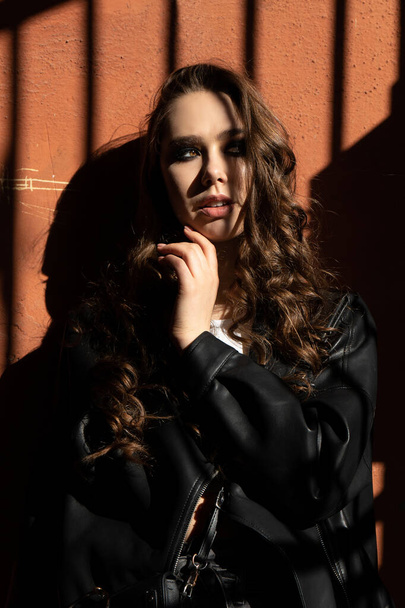 Εξωτερική πορτρέτο μιας νεαρής κομψής γυναίκας στο σκληρό φως με σκιές των αστικών φορώντας μοντέρνο μαύρο σακάκι με απίστευτο μακιγιάζ. Κλείσε. Χώρος κειμένου. - Φωτογραφία, εικόνα
