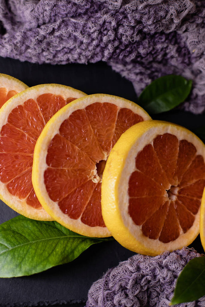 Grapefruit in Scheiben geschnitten auf einem schwarzen Teller und violettem Tuch und frischen jungen Blättern  - Foto, Bild