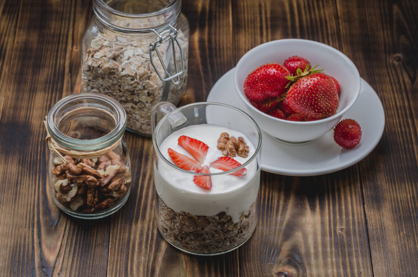 Healthy breakfast. Yogurt, fresh strawberry, homemade granola and walnut in open glass jar on a wooden tabl - Φωτογραφία, εικόνα
