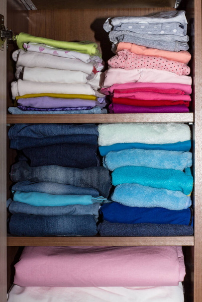 Neatly folded clothes on shelves in a closet at home. Wooden shelving with stacks of dark blue boy's and light pink and white clothes for the girl. Children's wardrobe, vertical photo. - Foto, imagen