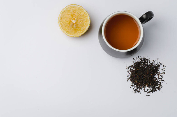 tea in a black mug, lemon segment and dried tea isolated on white background. Top view and copyspace - 写真・画像