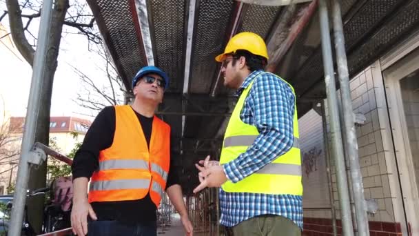 Δύο μηχανικοί με σκληρά καπέλα και ανακλαστικά μπουφάν ασφαλείας συζητούν στο εργοτάξιο - Πλάνα, βίντεο