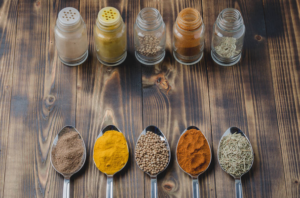 various spices in spoons and in glass jars on a wooden table. Ingredients for cooking. - 写真・画像