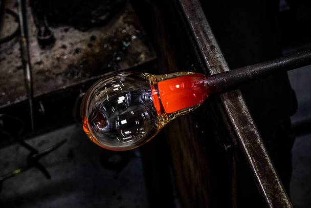Φυσητήρας γυαλιού που σχηματίζει όμορφο κομμάτι γυαλιού. Ένας υαλουργός καίγεται και ανατινάζει ένα έργο τέχνης. Φυσητήρας γυαλιού κάνει προσεκτικά το προϊόν του. Διαδικασία φυσήματος γυαλιού - Φωτογραφία, εικόνα