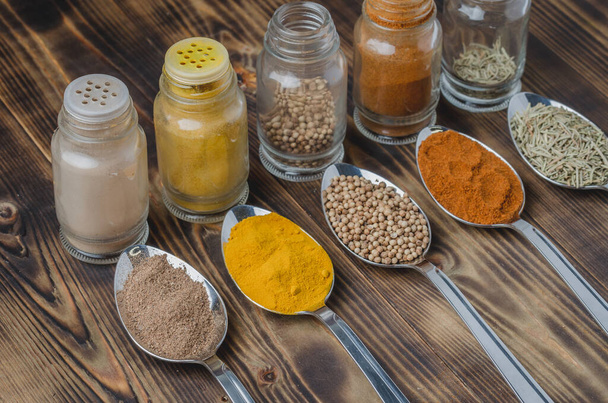 Colourful various spices in spoons and in glass jars on a wooden table. Cooking background. - Fotografie, Obrázek