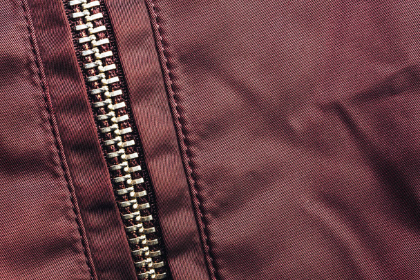 Nahaufnahme schöner Reißverschluss auf rotem Textilstoff Hintergrund mit Nähten. Makrofotografie Hintergrundmaterial Ansicht. - Foto, Bild