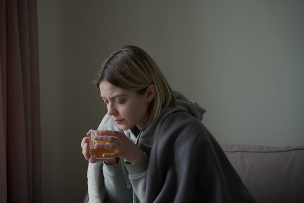 Sick woman drinks tea from a glass in light background - Foto, Imagen