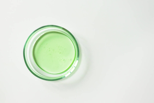 Transparentes grünes Shampoo oder Gesichtsreiniger in Glaspetrischale auf weißem Hintergrund, Ansicht von oben. Konzept Labortests und Forschung, Herstellung von Naturkosmetik - Foto, Bild