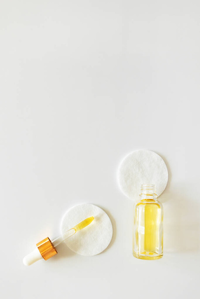 Vitamin E in glass bottle and pipette on cotton pads on white background, copy space. Skincare beauty product, above - Fotografie, Obrázek