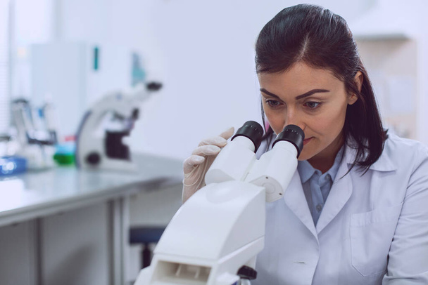 Concentrated female researcher looking into the microscope - Фото, изображение