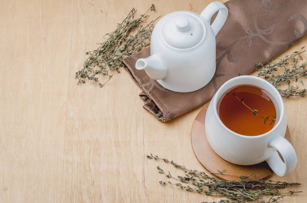 Thyme herbal tea in a white cup and teapot on a wooden table. Copyspace and top view - Photo, Image