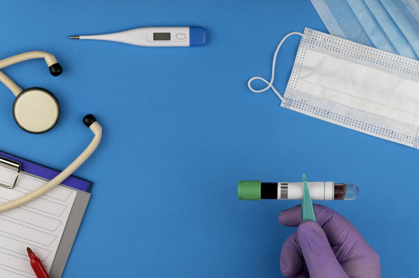 Platte lay compositie met bloedreageerbuis en elektronische thermometer op blauwe achtergrond. antiviraal medisch masker ter bescherming tegen het coronavirus COVID-19. barcode identificatie en registratie - Foto, afbeelding