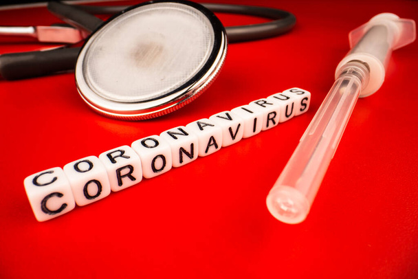 Πανδημία και την έννοια του ιού - Coronavirus κείμενο με σύριγγα και φωνοενδοσκόπιο σε κόκκινο φόντο. Μυθιστόρημα Coronavirus Covid-19. - Φωτογραφία, εικόνα