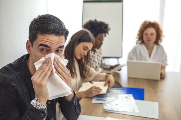 Cropped shot of a businessman suffering with allergies in an office. Shot of a frustrated businessman using a tissue to sneeze in while being seated in the office. Working when sick - Фото, изображение