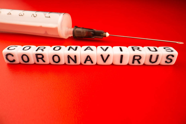 Pandemický a virový koncept - Koronavirový text s injekční stříkačkou na červeném pozadí. Novel coronavirus Covid-19. - Fotografie, Obrázek