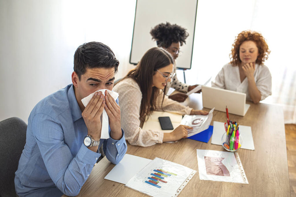 Cropped shot of a businessman suffering with allergies in an office. Shot of a frustrated businessman using a tissue to sneeze in while being seated in the office. Working when sick - Foto, afbeelding