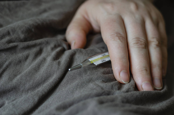 Female hand lies on a blanket. In his hand is a mercury thermometer. The concept is bed rest, treatment, temperature measurement. Eye level shooting. Selective focus. - Fotó, kép