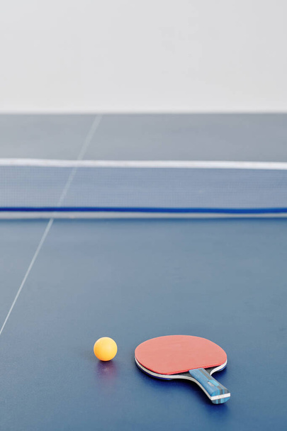 Racchetta da ping pong e palla arancione sul tavolo divisa in due metà da una rete, focalizza l'attenzione sul primo piano - Foto, immagini