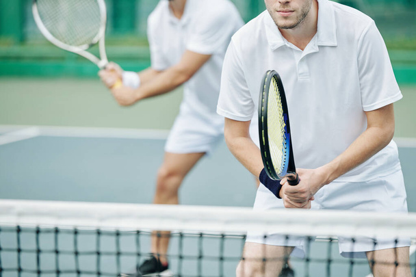 Gehakt beeld van geconcentreerde jonge tennisser staan aan het net en klaar om de bal te raken - Foto, afbeelding