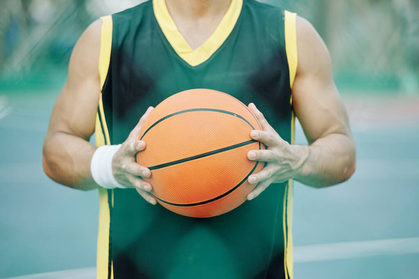 Balle de basket entre les mains d'un joueur debout sur un terrain extérieur - Photo, image
