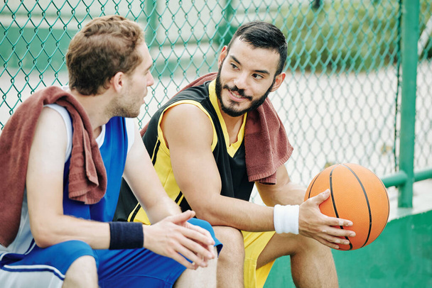 Улыбающийся латиноамериканец разговаривает с другом после игры в баскетбол на открытом воздухе - Фото, изображение