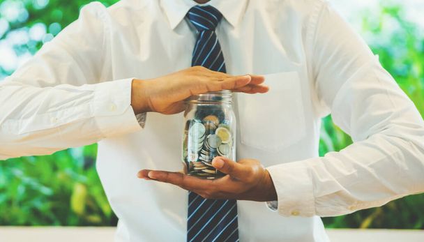 Бизнесмен держит монеты в стекле. Экономия денег
. - Фото, изображение