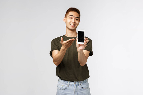 テクノロジー、オンラインライフスタイル、コミュニケーションの概念。喜んで陽気なアジア人の男性の肖像画は、彼のゲームのスコアとブログ、携帯電話のアプリケーションを紹介スマートフォンのディスプレイを表示します。 - 写真・画像