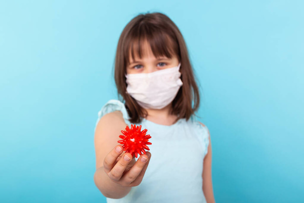 Virus, Pandemie, Quarantäne und Ausbruchskonzept - Kleines Mädchen lässt sich mit medizinischer Maske vor Coronavirus schützen COVID-19 hält Modell des Coronavirus. - Foto, Bild